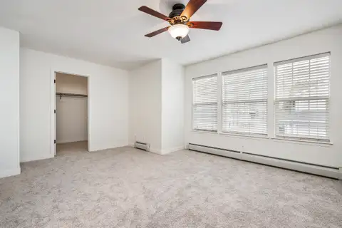 Bedroom with three windows, a ceiling fan, new carpet and a walk-in closet