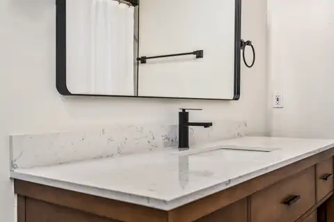 Close-up of a wood vanity with a white stone-look countertop, black faucet and black-framed mirror