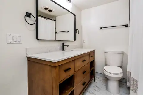 Hall bathroom with a wood vanity, white stone-look top, black faucet and tile floor