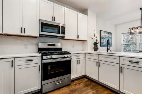 L-shaped kitchen with white cabinets, stainless gas range and over-the-range microwave