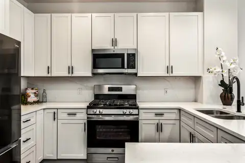 Kitchen range wall with white shaker cabinets, black pulls, stainless microwave and gas range