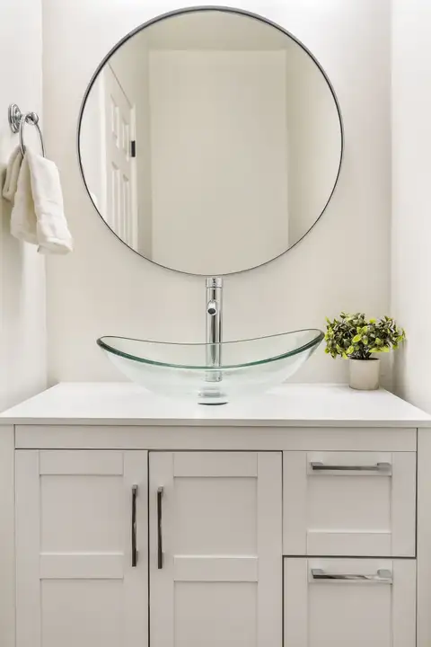 Powder room with a glass vessel sink on a white shaker vanity and a round mirror
