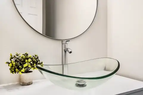 Glass vessel sink and brushed nickel faucet under a round mirror