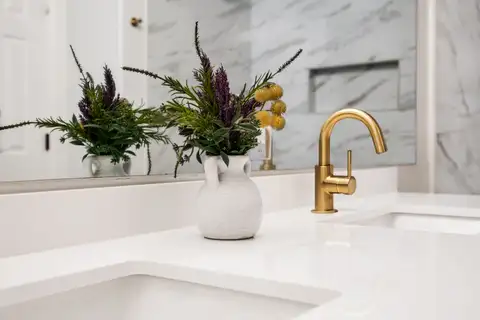 Brass faucet and undermount sink on a white vanity top with tile shower behind