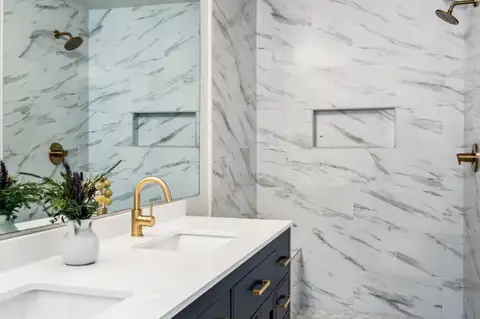 Walk-in shower with large marble-look wall tile, a recessed niche and brass shower fixtures