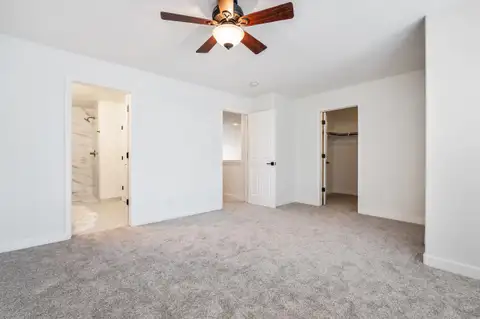 Primary bedroom with new carpet, a ceiling fan and doors to the bathroom and walk-in closet